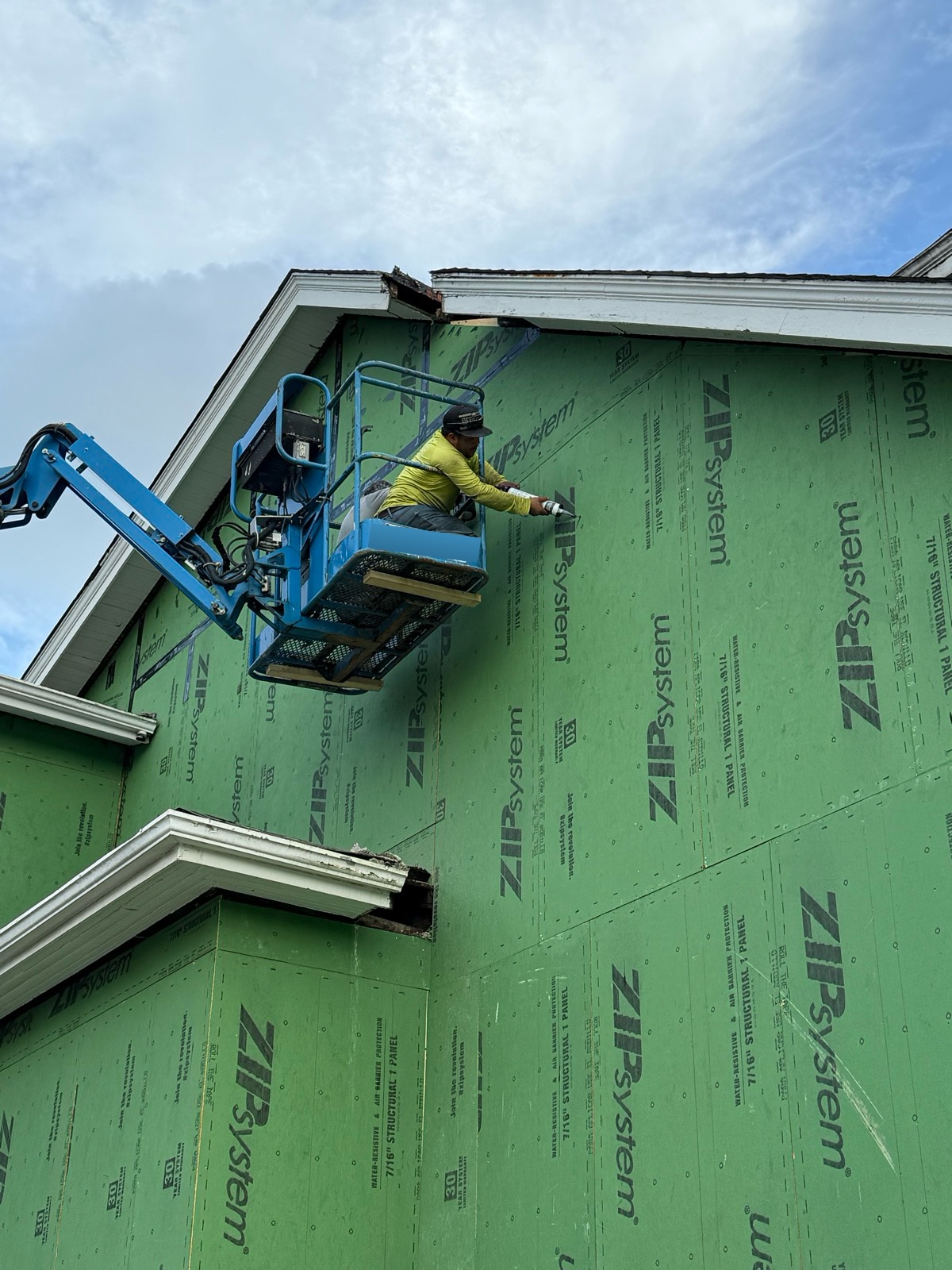 An M3G crew member on a lift sealing the seams of new exterior sheathing