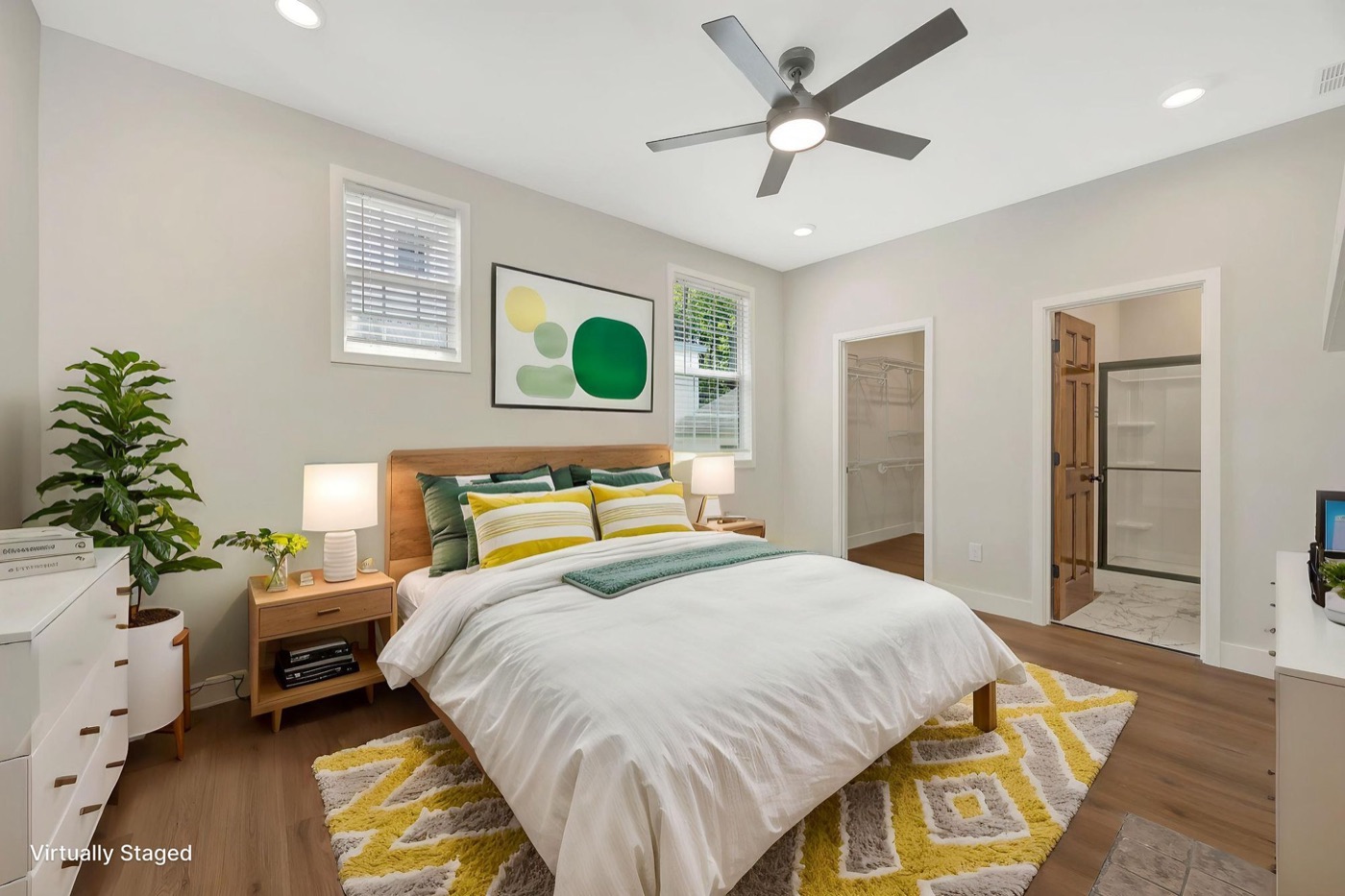 A bedroom in a new M3G home with a ceiling fan, walk-in closet and attached bathroom, shown virtually staged with furniture