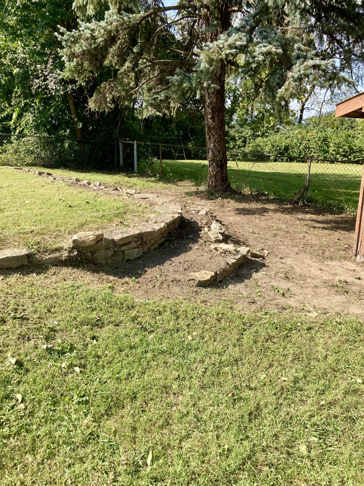 A stacked stone border being set along a backyard bed under an evergreen tree