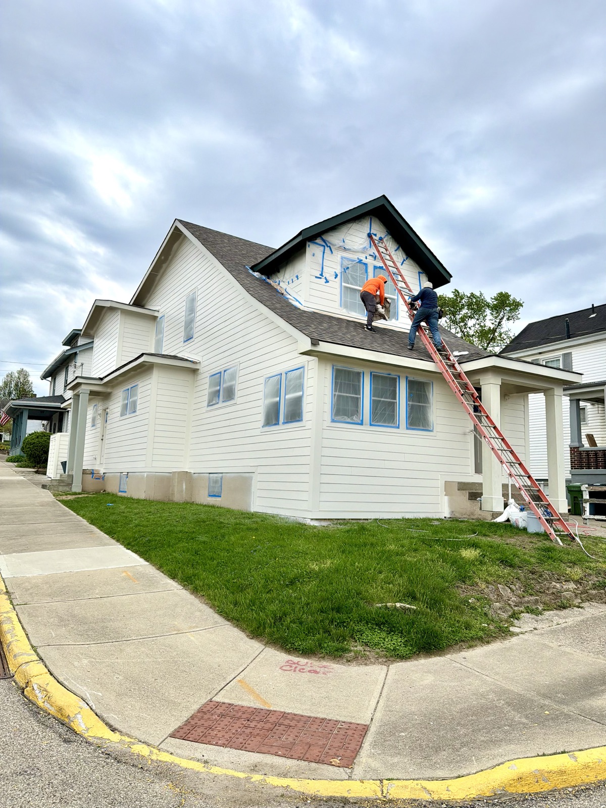 Two M3G painters on a ladder painting the gable of a white two-story house
