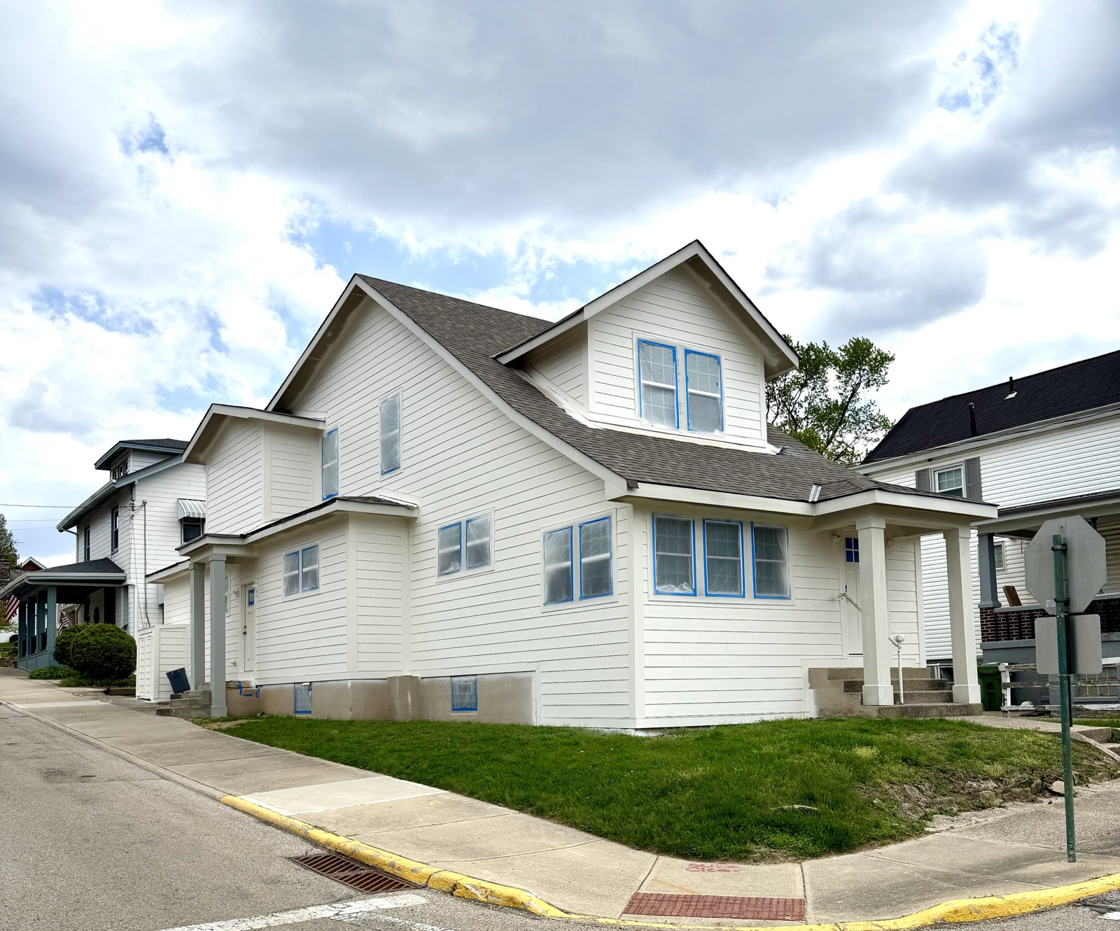 A freshly painted white two-story house with blue-trimmed windows on a corner lot