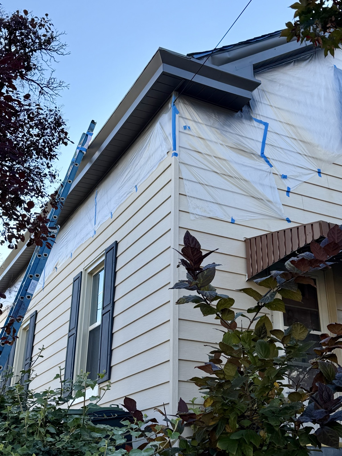 Siding and trim masked in plastic and blue tape before exterior painting