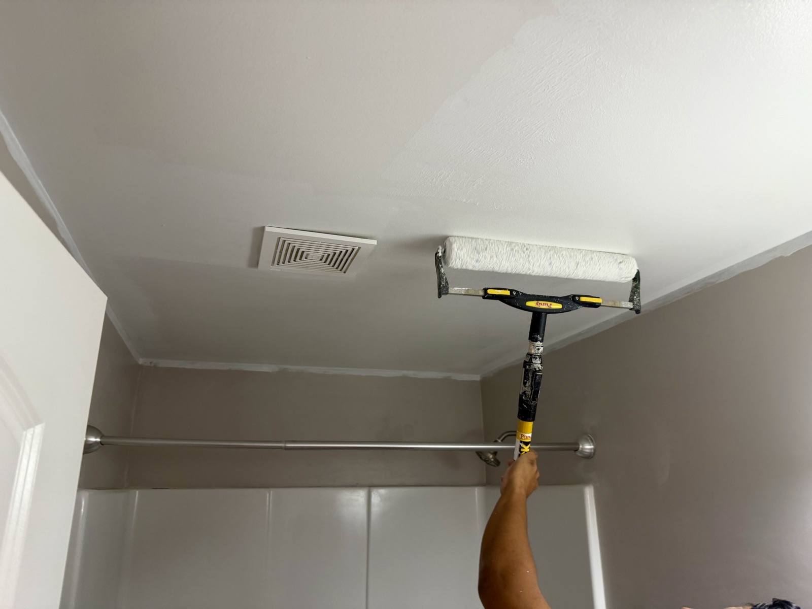 A painter rolling white paint onto a bathroom ceiling