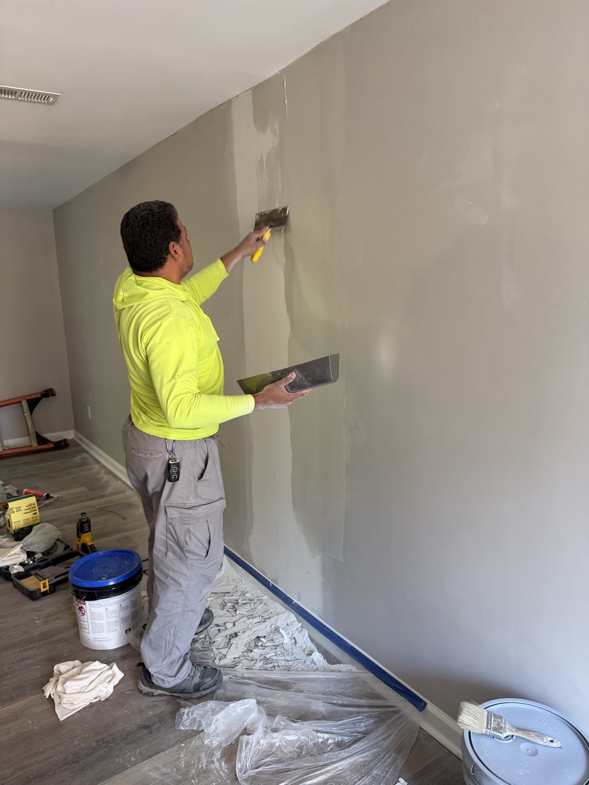An M3G painter smoothing an apartment wall with a drywall knife before painting