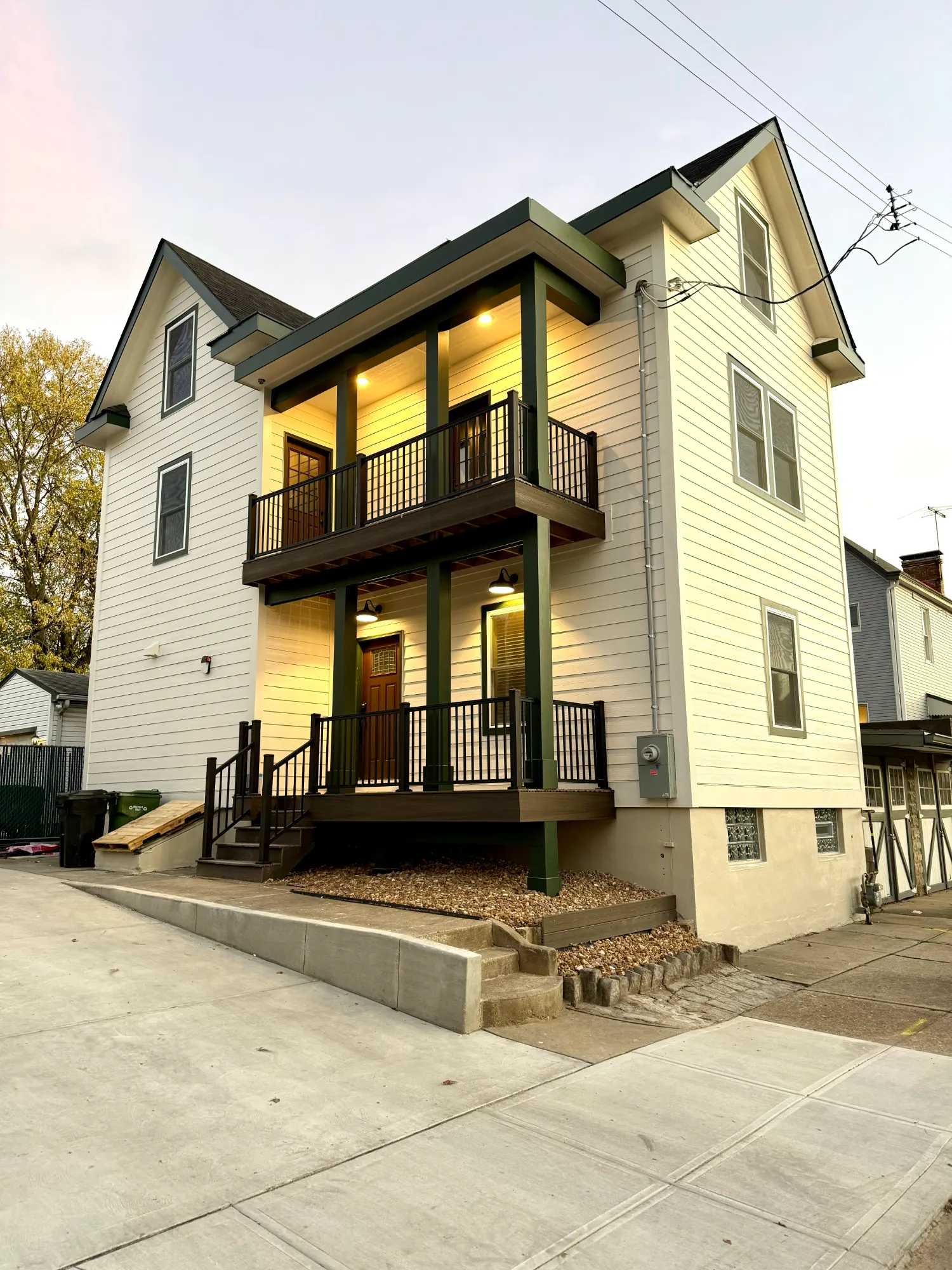After: the same house with new cream siding, green trim and a rebuilt two-story porch with lights on
