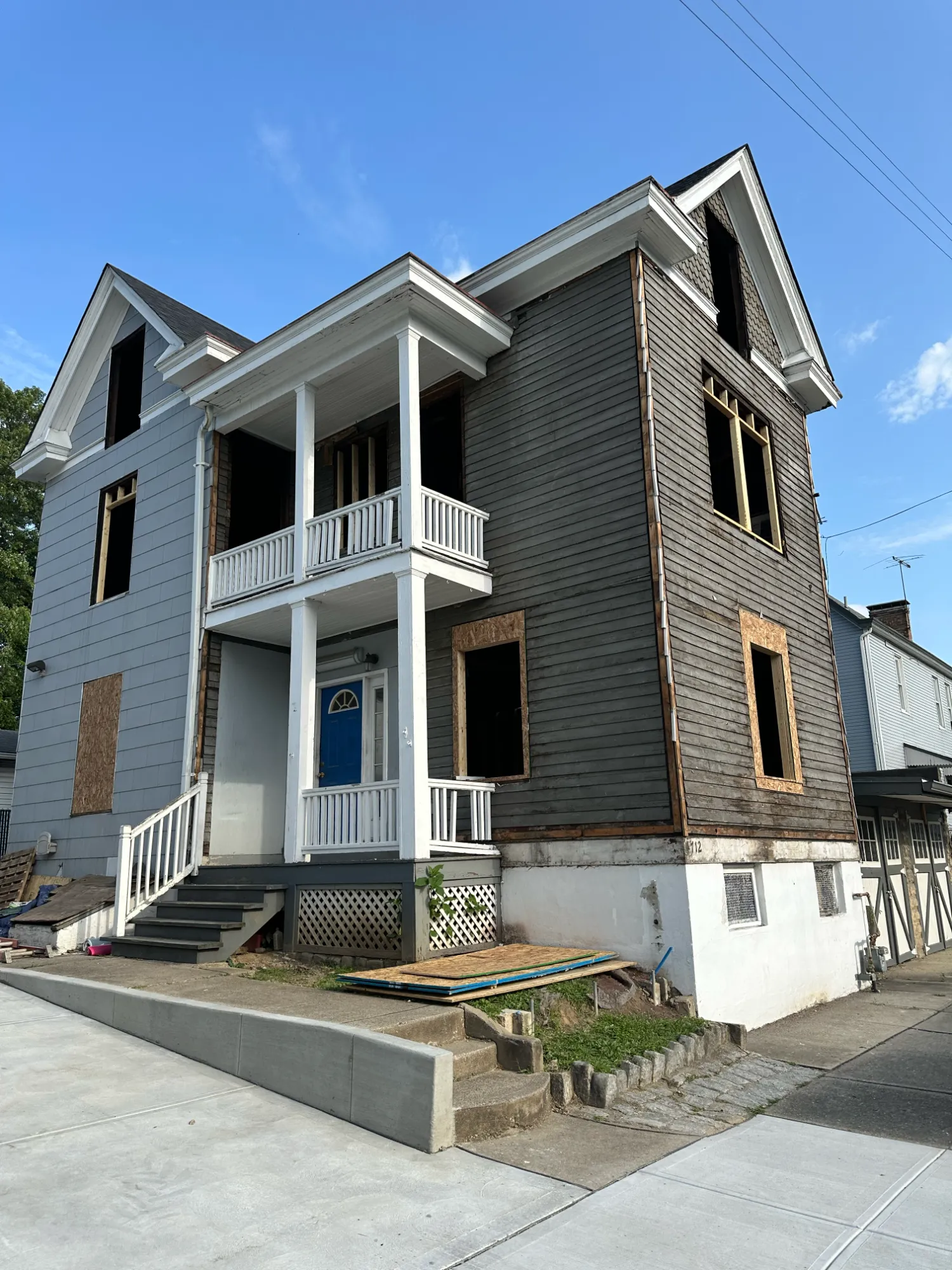 Before: a three-story house mid-rehab with stripped siding, open window frames and boarded windows
