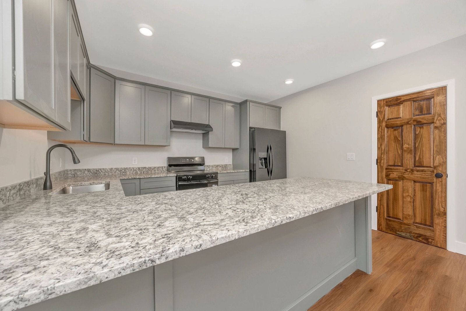 A renovated kitchen with gray cabinets, granite counters and a peninsula