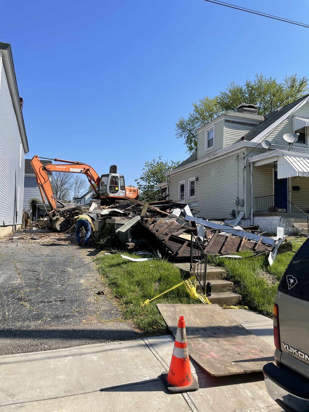 An excavator knocking down an old house, with a worker clearing debris