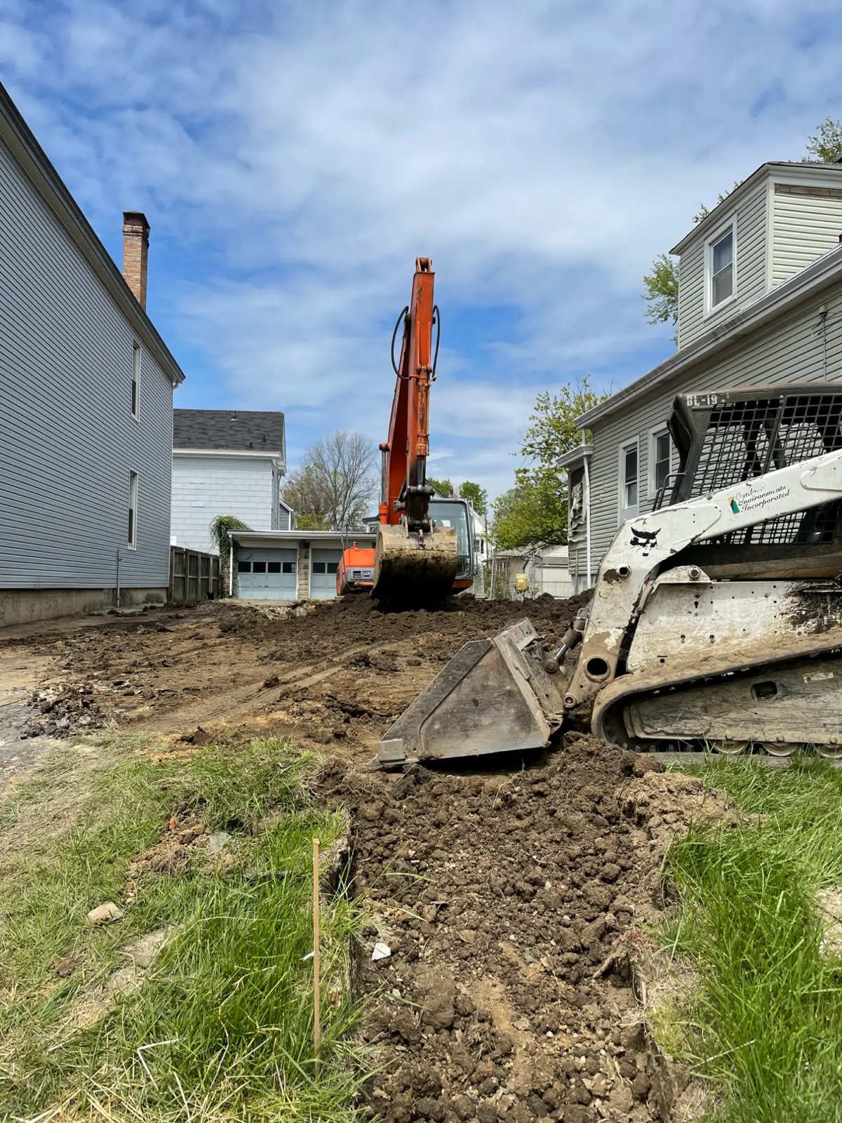 An excavator and skid steer grading a cleared city lot between two houses