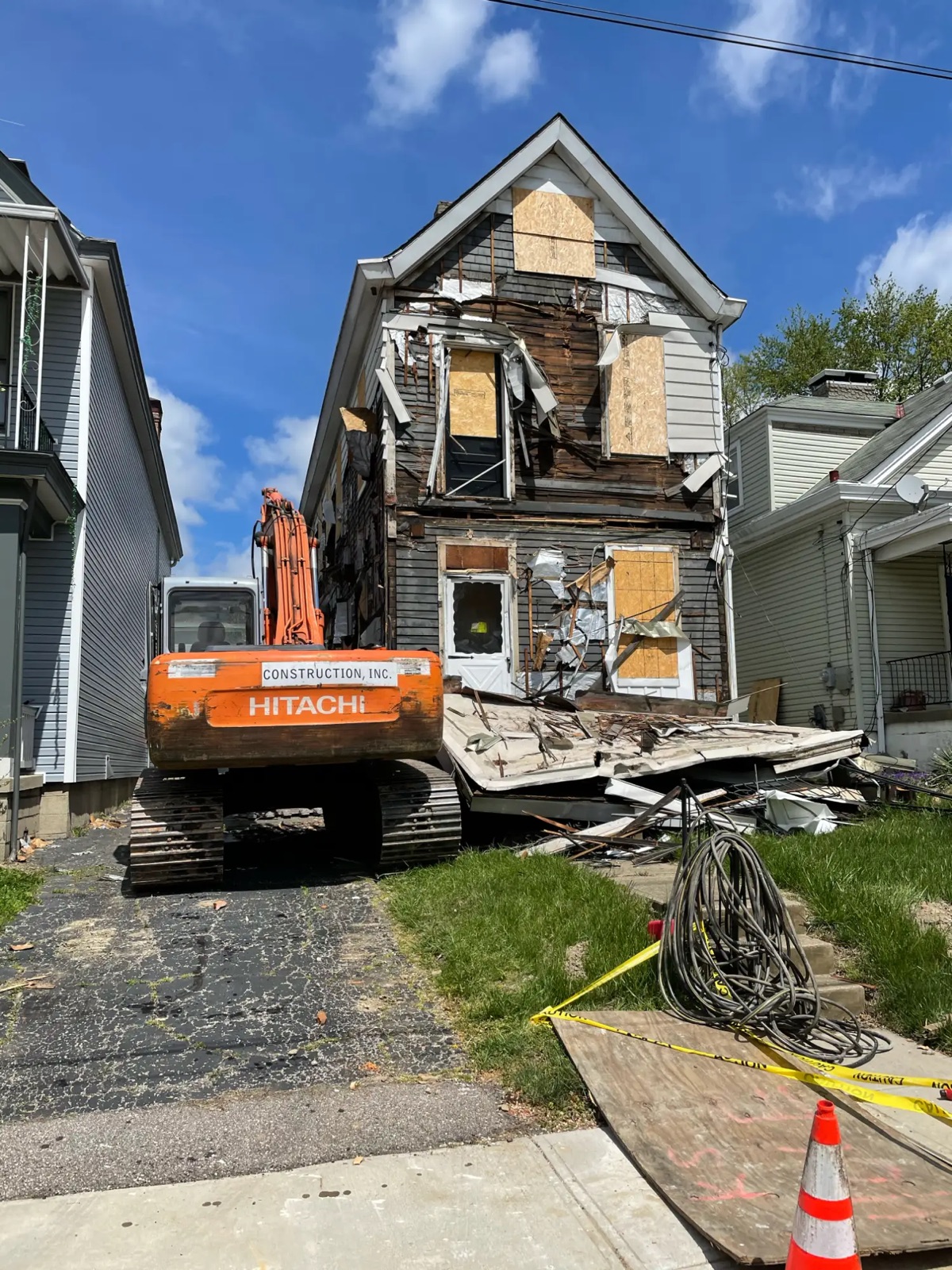 An excavator starting on a run-down, boarded-up two-story house between two neighbors