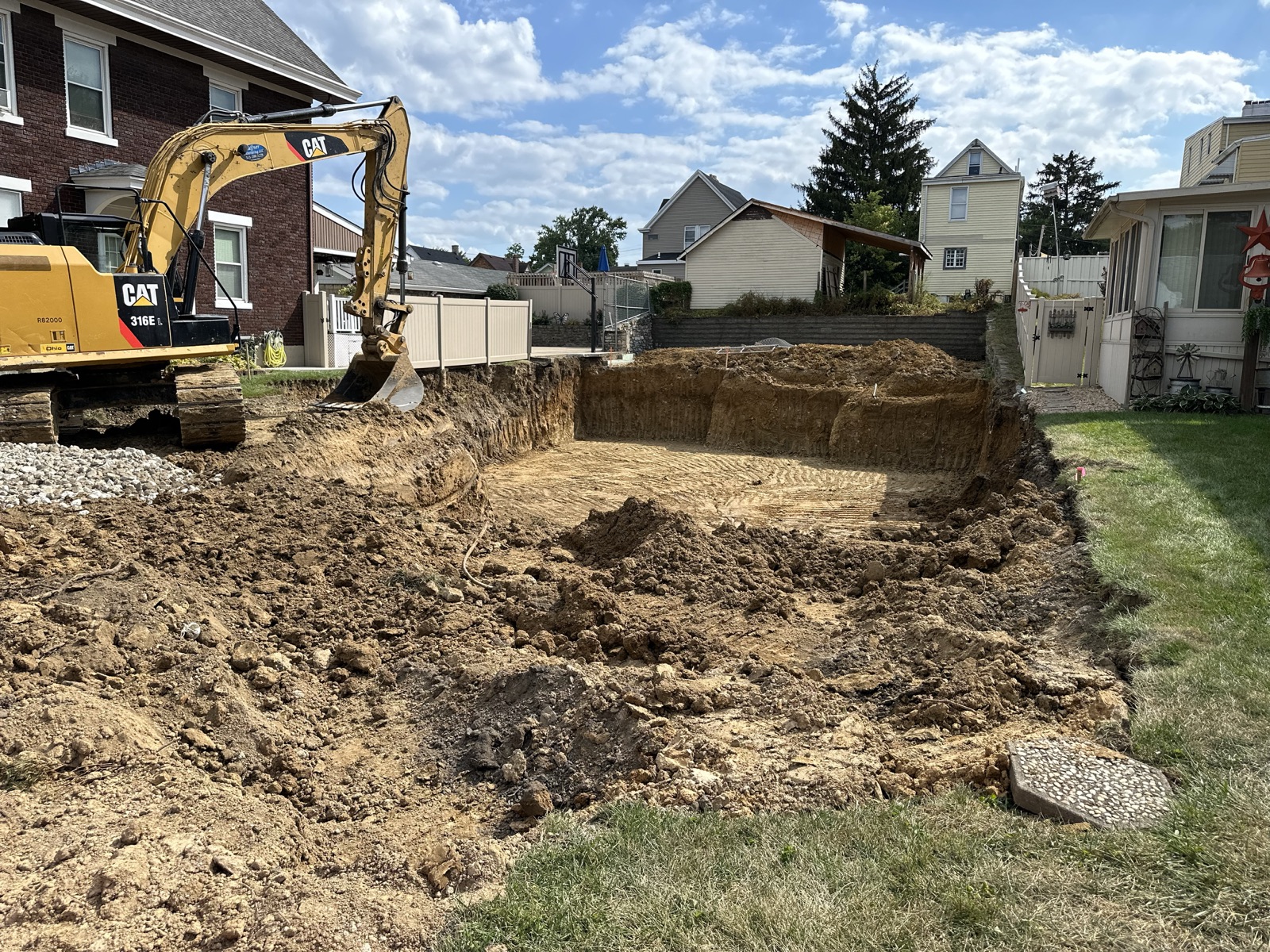 A CAT excavator digging out the basement for a new home between neighboring houses