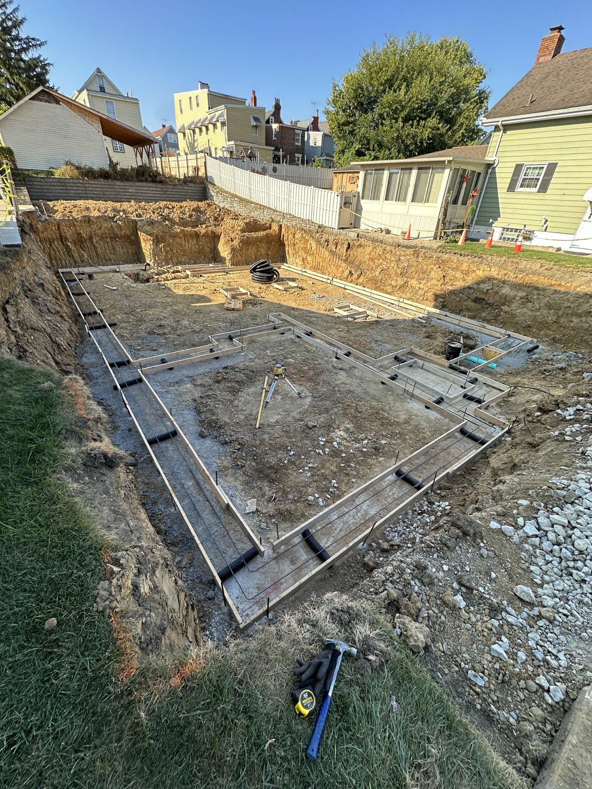 Footing forms and rebar laid out in a dug basement, with a laser level set up in the middle