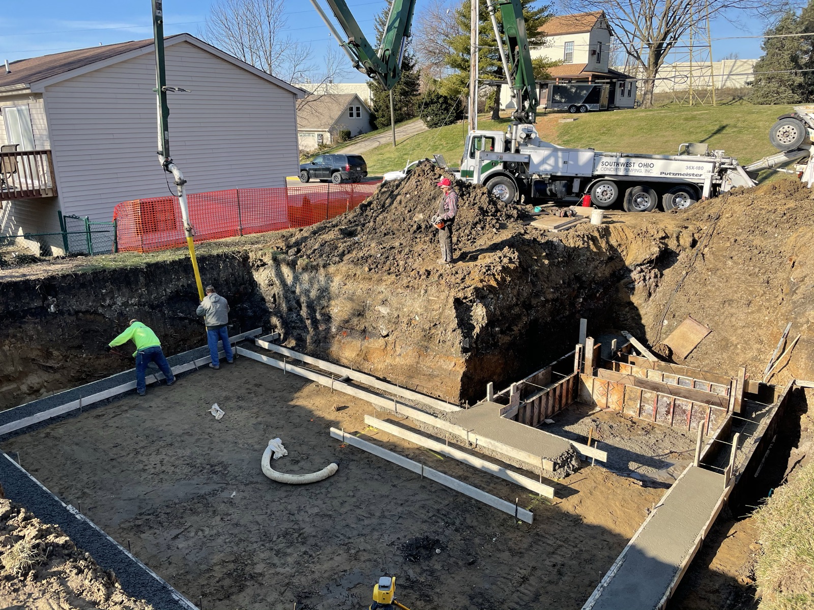 A crew pouring footings in a basement excavation while a concrete pump truck reaches in