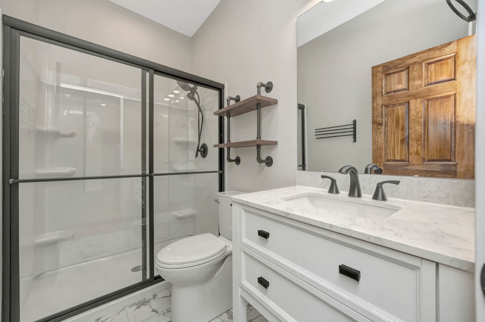 A bathroom with a glass walk-in shower, white vanity, marble-look top and black fixtures