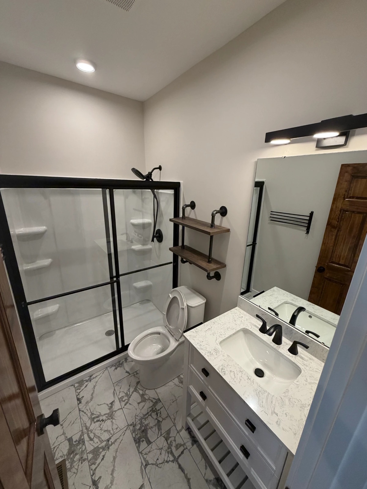 A bathroom with a white vanity, black fixtures, glass shower doors and marble-look tile floors