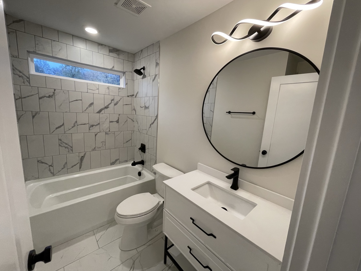 A new bathroom with a marble-look tub surround and round mirror