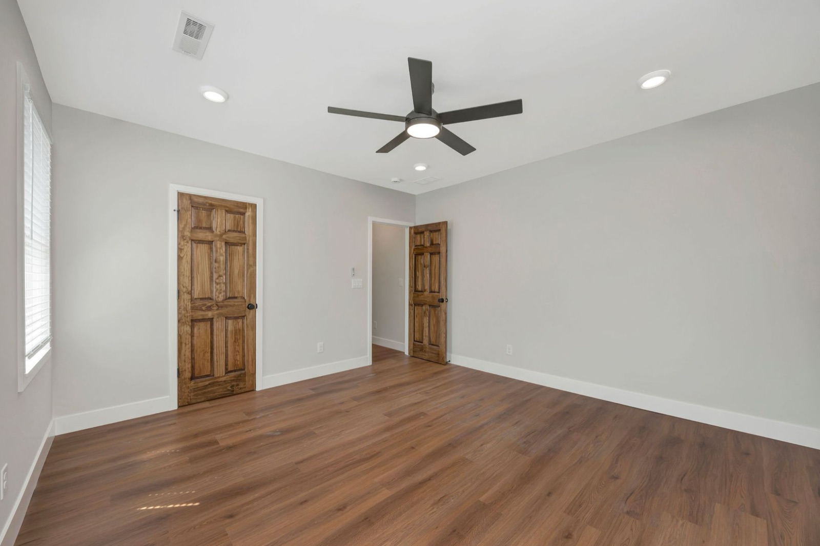 A second bedroom with a stained closet door, plank floors and a ceiling fan