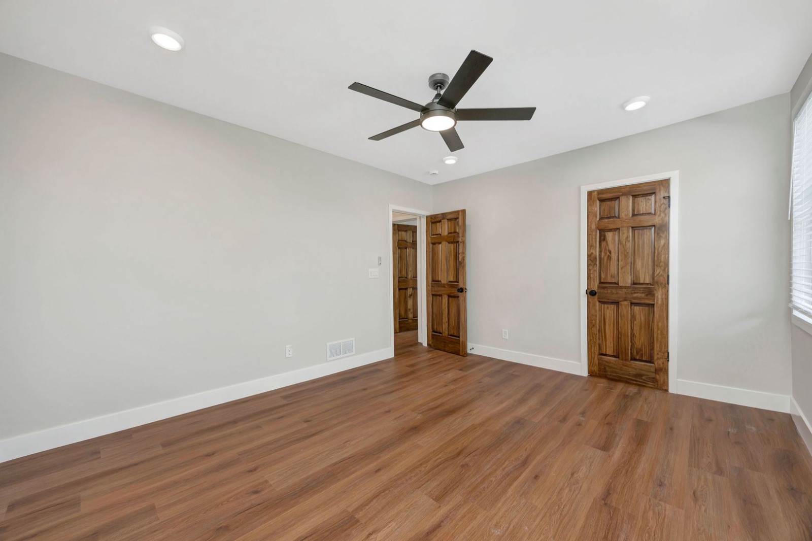 A bedroom with stained six-panel doors, plank floors and a ceiling fan