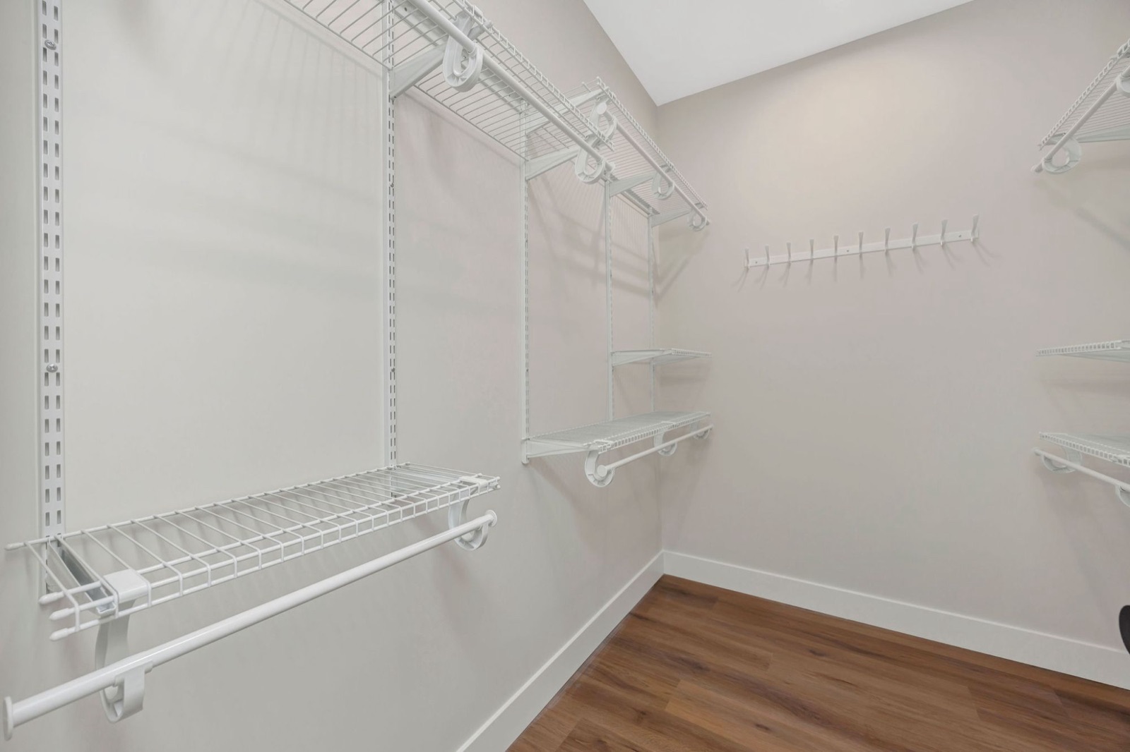 A walk-in closet with white wire shelving, hanging rods and a row of hooks