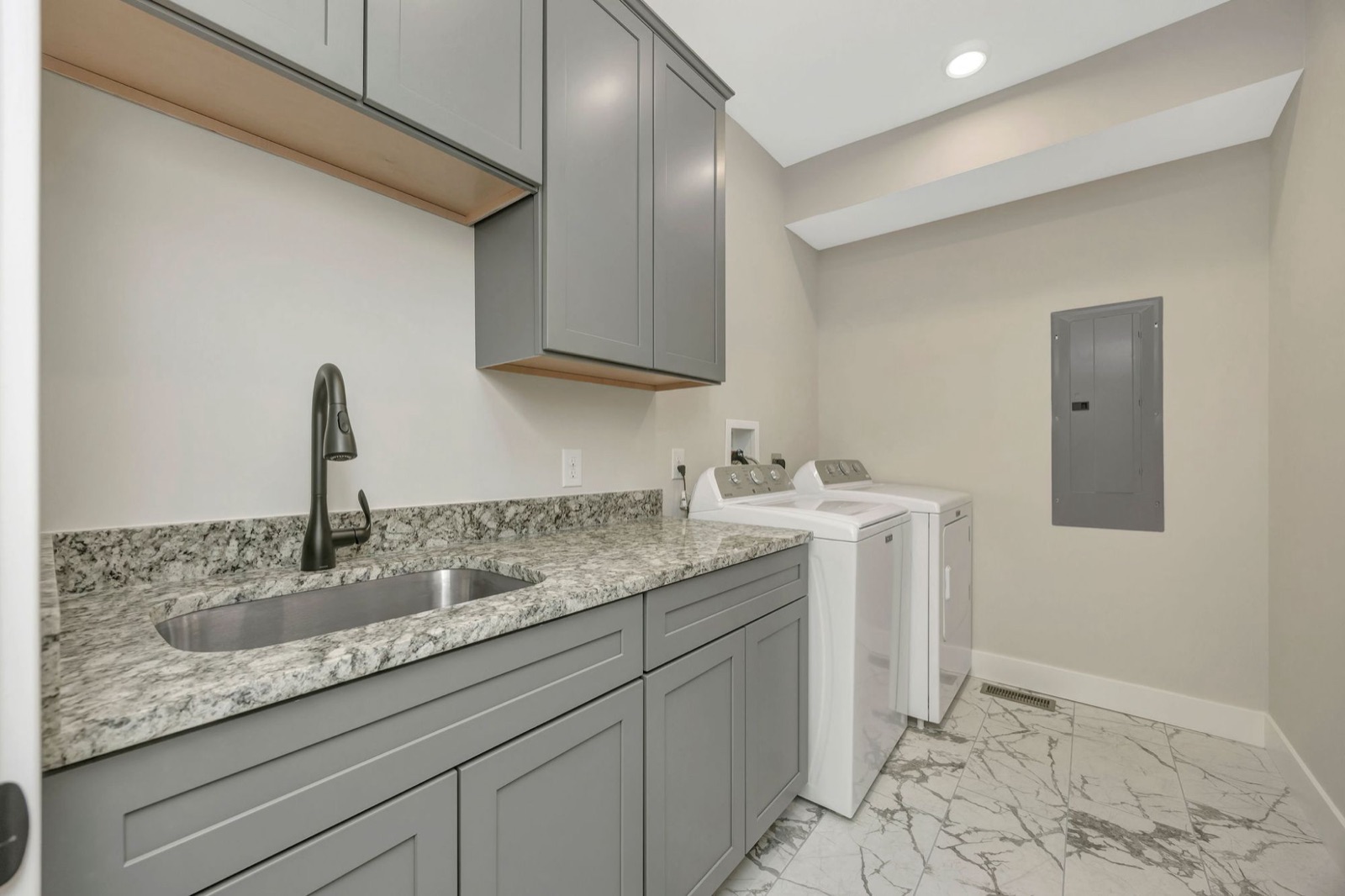 A laundry room with gray shaker cabinets, a granite counter, an undermount sink and a washer and dryer