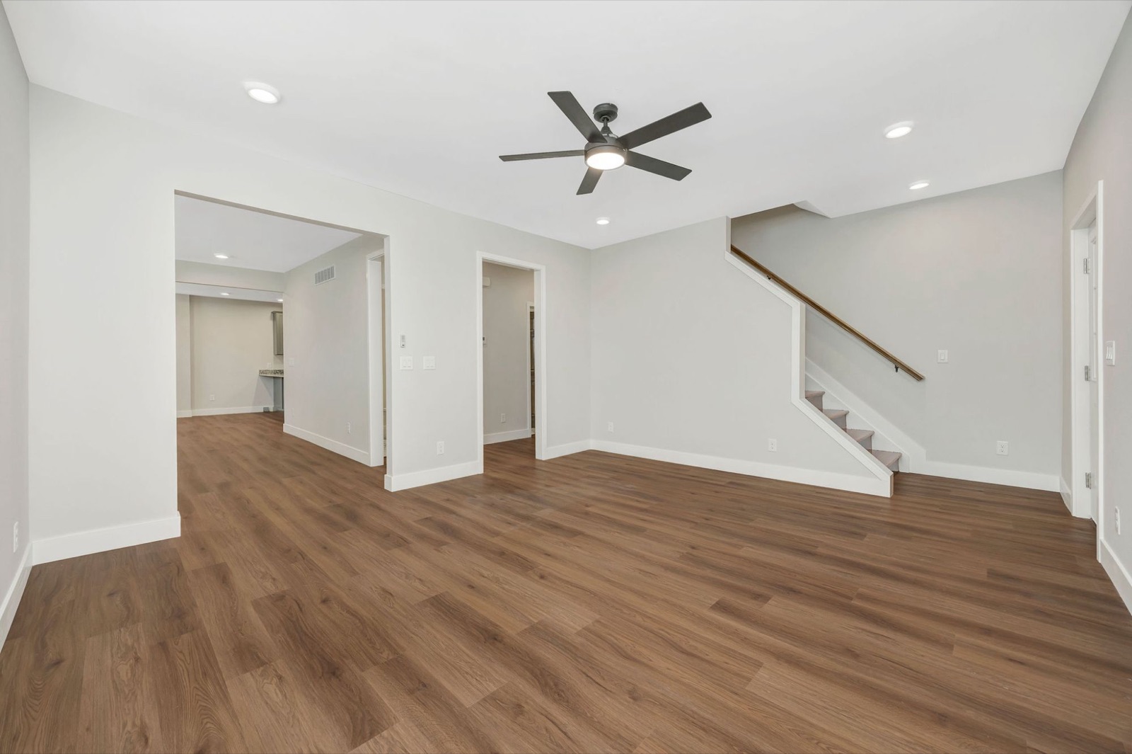 An open living room with wood-look plank floors, recessed lights, a ceiling fan and a staircase