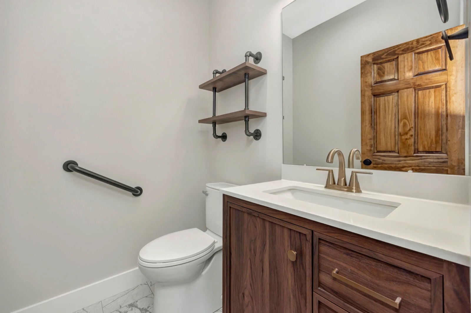A half bath with a walnut vanity, white quartz top, brass faucet and pipe shelving