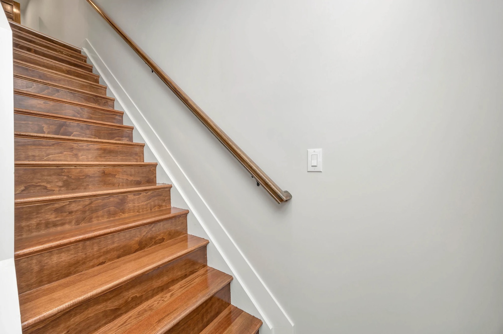 A stained wood staircase with a matching handrail along a white wall